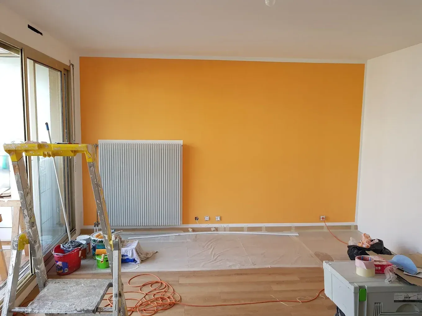 Chantier de peinture intérieure : mur orange vif, protection du sol et finitions soignées